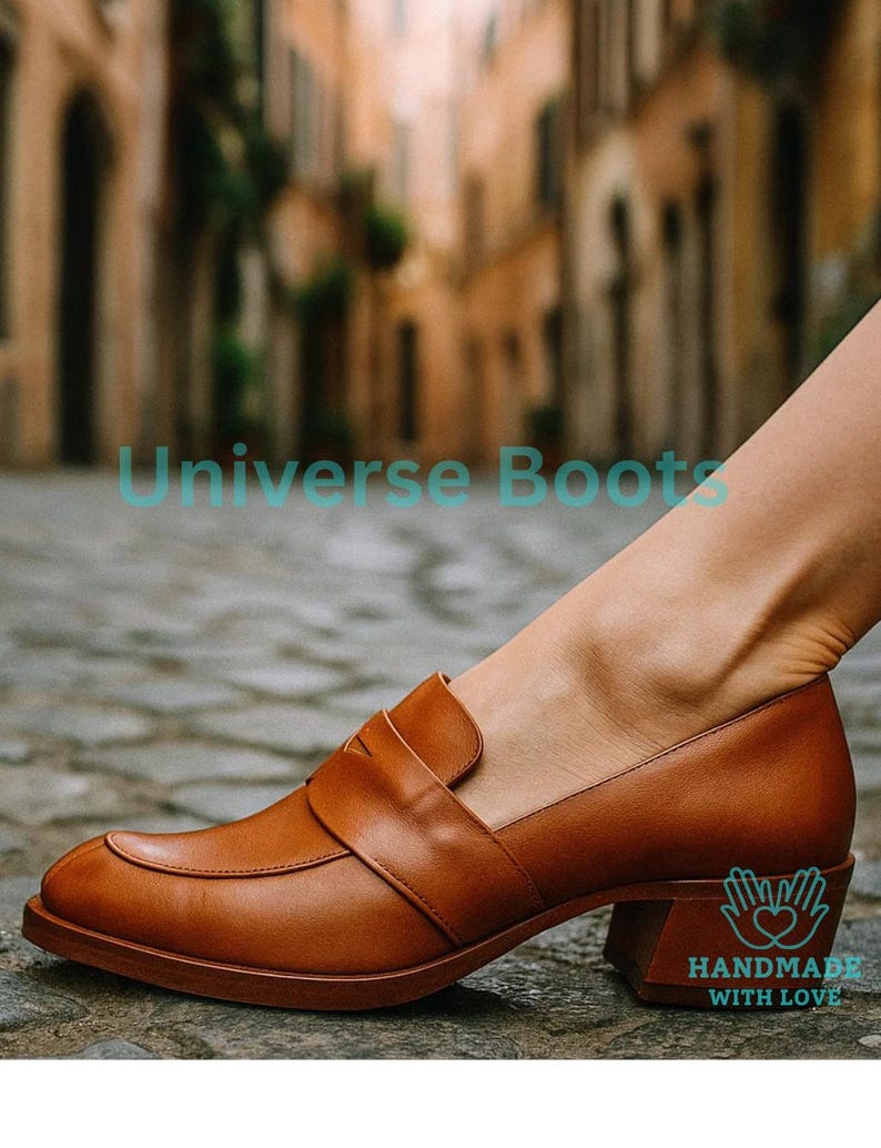 May include: Tan leather loafers with a block heel. The shoes feature a classic design with a strap across the top. The image also includes the text "Universe Boots" and "HANDMADE WITH LOVE".
