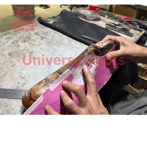 Op de afbeelding: Een houten schoenleest met een roze papieren patroon. De tekst "HANDMADE WITH LOVE" en "Universal Boots" zijn zichtbaar. De afbeelding toont het proces van schoenmaken.