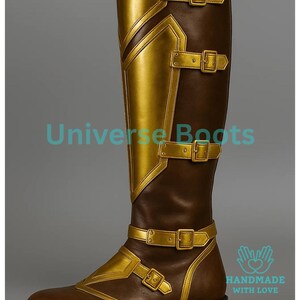 May include: Brown and gold knee-high boot with buckle details. The boot features gold accents on the front and sides, with multiple buckles and straps. The boot has a zipper on the back and is labeled "Universe Boots" and "Handmade with Love".