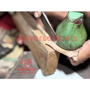 Op de afbeelding: Een close-up van de handen van een schoenmaker die leer bewerkt. De afbeelding toont een houten leest, een groen gereedschap en een mes dat wordt gebruikt om het leer te vormen. De tekst "Universe Boots" en "Handmade with Love" zijn zichtbaar.