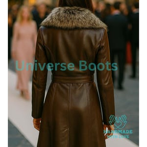 Puede incluir: Un abrigo de cuero marr&oacute;n con cuello de piel sint&eacute;tica y cintur&oacute;n en la cintura. El abrigo tiene mangas largas y una falda acampanada. El texto "Universe Boots" es visible en la parte inferior izquierda de la imagen. Tambi&eacute;n son visibles las palabras "HANDMADE WITH LOVE".