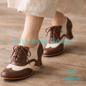May include: Brown and cream-colored Oxford-style shoes with a lace-up design. The shoes have a wingtip design and a stacked heel. The shoes are made of leather and have a classic, vintage look. The shoes are a size 8.
