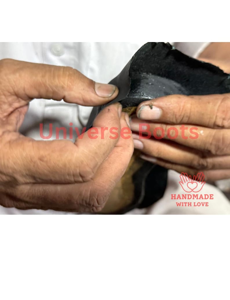 Op de afbeelding: Close-up van handen die aan een zwart lederen item werken. De tekst "Universe Boots" is in het rood zichtbaar, samen met een "Handmade with Love" logo.