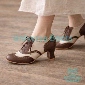 May include: Brown and cream-colored oxford-style shoes with a low heel. The shoes have a lace-up design and a classic wingtip pattern. The heels are approximately 2 inches high. The shoes are made of leather and have a vintage aesthetic.