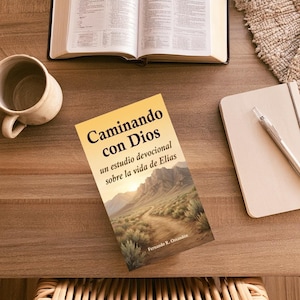 May include: A book titled Caminando con Dios, un estudio devocional sobre la vida de Elias by Fernando R. Ossandón, featuring a cover illustration of a dirt path leading towards mountains under a bright sun, placed on a wooden desk surface.