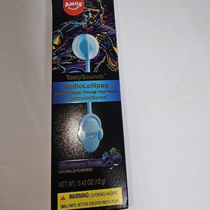 May include: A package for a blueberry-flavored AudioLollipop. The black box features a graphic of a person and a blue lollipop. The text reads "TastySounds AudioLollipop" and "Listen to Music Through Your Mouth Electronic/Dance". The net weight is 0.42 oz (12 g).
