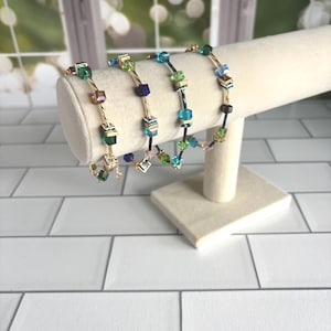 Puede incluir: Cuatro pulseras con una base de alambre de metal dorado trenzado adornadas con cuentas c&uacute;bicas de varios colores. Las cuentas incluyen tonos verdes, azules, rosas y marr&oacute;n oscuro, intercaladas con peque&ntilde;os espaciadores met&aacute;licos a lo largo de cada pulsera.