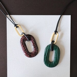 May include: Two necklaces with black cords and oval-shaped pendants. One pendant is dark brown with a snakeskin pattern, the other is green with a crocodile skin pattern.