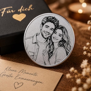 Könnte beinhalten: Eine runde Metallscheibe mit einem lasergravierten Porträt eines lächelnden Paares. Die Scheibe liegt neben einer schwarzen Geschenkbox mit dem goldenen Text Für dich und einem Herzsymbol sowie einer beigen Karte mit dem Text Kleine Momente. Große Erinnerungen.