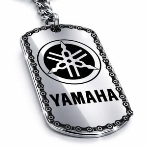 Peut inclure: Un porte-clés Yamaha argenté avec une bordure en forme de chaîne. Le porte-clés présente le logo Yamaha noir dans un cercle et le mot "YAMAHA" imprimé en dessous.