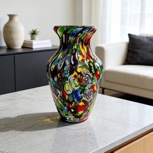 May include: A colorful glass vase with a wide, flared top. The vase features a vibrant pattern of red, yellow, blue, and green glass pieces. The vase is a decorative item, suitable for displaying flowers or as a standalone art piece.