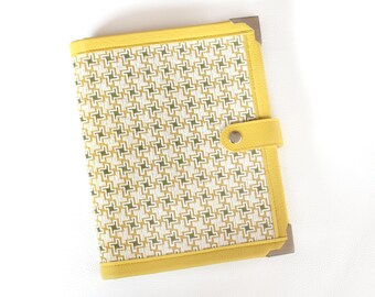 Può includere: Una cartella in pelle gialla con un motivo geometrico verde e bianco. La cartella ha una chiusura in metallo e una patta con un bottone.