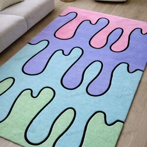May include: A colorful area rug with a unique design. The rug features a pattern of flowing shapes in shades of pink, purple, blue, and green, outlined in black. The rug is rectangular and appears to be made of a soft material.