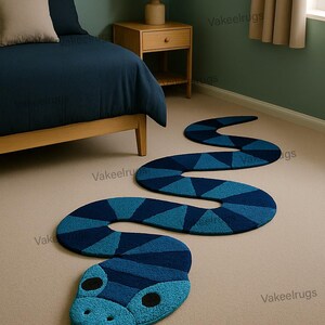 May include: A blue snake-shaped rug with a geometric pattern, placed on a beige carpet. The rug's head features a light blue face with black eyes and a red tongue. The rug is near a bed with navy blue bedding.