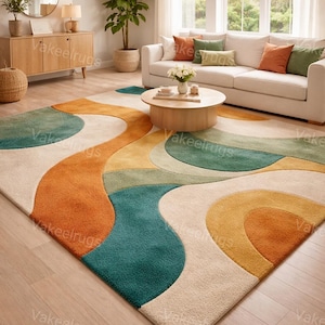 May include: A large, colorful area rug with an abstract design in shades of orange, teal, yellow, green, and cream. The rug is placed in a living room setting with a white sofa, wooden coffee table, and large windows.