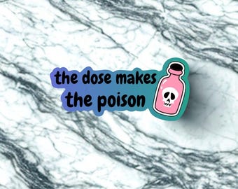 May include: A sticker with the text "the dose makes the poison" and a pink poison bottle with a skull graphic. The sticker has a teal border and a gradient blue and purple background. The background is a marble pattern.
