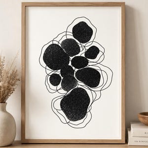 May include: Abstract art print with a cluster of black, textured shapes and thin, looping black lines on a white background. The artwork is framed in a light brown wooden frame, suitable for home decor.