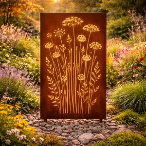 May include: A rectangular, weathered metal garden screen featuring a floral design. The screen has a rusty brown color with a cut-out pattern of tall, slender plants with delicate, round flower heads. The screen is set in a garden with various plants and flowers.