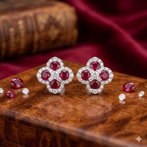 Könnte beinhalten: Ein Paar kleeblattförmige Ohrstecker mit vier rund geschliffenen roten Rubinen, umgeben von einem Kranz aus kleinen weißen Diamanten. Mehrere lose runde Rubine und kleine weiße Diamanten liegen verstreut um die Ohrringe auf einer Holzoberfläche.