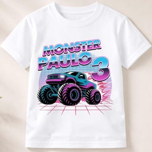 Puede incluir: Camiseta blanca con un gr&aacute;fico colorido de un monster truck y el texto "MONSTER PAULO 3". El dise&ntilde;o incluye un monster truck azul y morado con neum&aacute;ticos grandes, sobre un fondo retro.