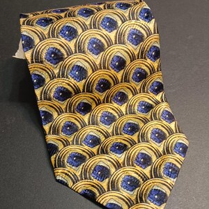 Peut inclure: Cravate à motifs avec un motif répété de demi-cercles dorés et noirs avec des accents floraux bleus. La cravate est pliée. Un accessoire classique, probablement en soie ou dans une matière similaire.