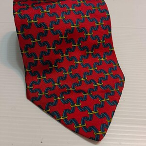 以下が含まれることがあります： 赤色のネクタイ。青と黄色の鎖のようなデザインが繰り返されています。滑らかな生地で作られており、フォーマルまたはビジネスシーンに適しています。