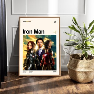May include: Framed movie poster for "Iron Man" featuring the film's title in bold black letters. The poster showcases the main characters in costume against a vibrant, colorful background. The year 2010 is printed in the bottom right corner.
