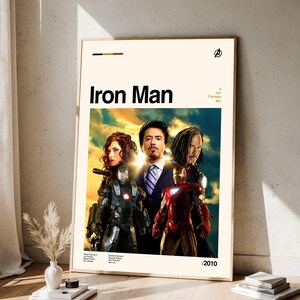 May include: A framed movie poster for "Iron Man" featuring the film's title in bold black letters. The poster showcases images of the main characters, including Iron Man in his red and gold suit, and other actors. The poster is set against a cream background.