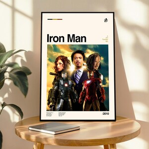 May include: Framed poster featuring the movie "Iron Man" with actors Robert Downey Jr., Gwyneth Paltrow, and Don Cheadle. The poster has a cream-colored background with the title "Iron Man" in bold black letters. The year 2010 is printed at the bottom.