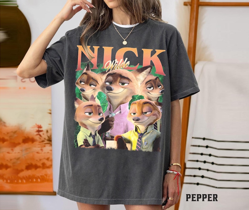 May include: Dark gray t-shirt featuring a graphic of Nick Wilde from Zootopia. The design includes the name "Nick Wilde" in orange and the character's image. The shirt is a casual, oversized fit.