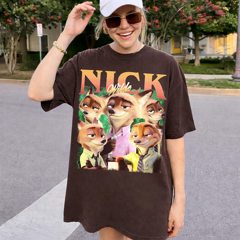 May include: Brown t-shirt featuring the text "Nick Wilde" in orange and a graphic of several cartoon foxes. The foxes are wearing shirts and ties. The shirt is a casual, oversized fit.