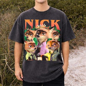 May include: Dark gray t-shirt featuring a graphic of Nick Wilde from Zootopia. The design includes the text "NICK Wilde" in orange and white, with images of Nick Wilde in various poses. The shirt has a vintage, distressed look.