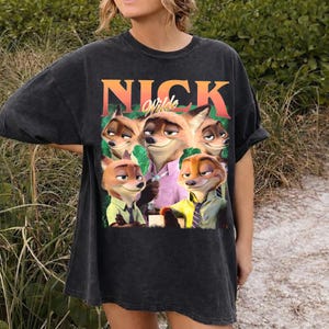 May include: Black t-shirt featuring a graphic of the animated character Nick Wilde from the movie Zootopia. The image shows Nick Wilde and other fox characters. The word "NICK" is printed above the image in orange and green.