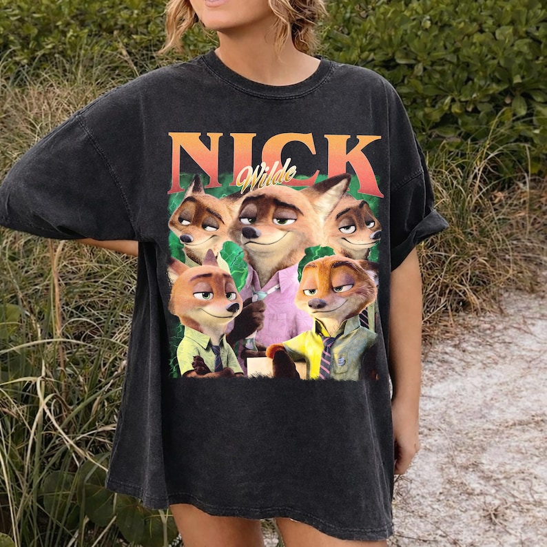 May include: Black t-shirt featuring a graphic of the animated character Nick Wilde from the movie Zootopia. The image shows Nick Wilde and other fox characters. The word "NICK" is printed above the image in orange and green.