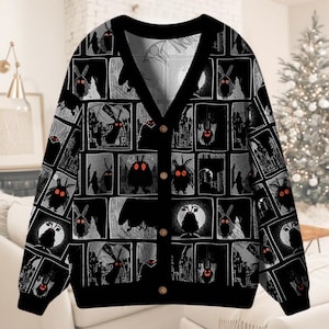 Könnte beinhalten: Schwarze Strickjacke mit einem sich wiederholenden Comic-Muster, das ein mottenartiges Wesen mit leuchtend roten Augen zeigt. Die Strickjacke hat einen V-Ausschnitt, einen Knopfverschluss und einen schwarzen Hintergrund mit grauen und weißen Illustrationen.