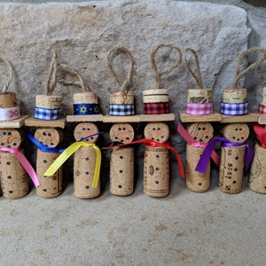 May include: Nine cork snowman ornaments with different colored hats and scarves. The hats are plaid, gingham, and solid colors. The scarves are pink, yellow, blue, purple, and red.