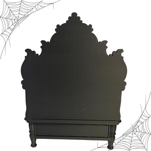 May include: A black, ornate, decorative cabinet with a drawer and decorative legs. The cabinet has a detailed, curved top. Spiderwebs are in the background. This cabinet is perfect for Halloween decor.