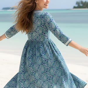 Knee-length blue and green paisley print dress with a V-neckline, three-quarter sleeves, gathered waist, and flowy flared skirt in lightweight fabric.
