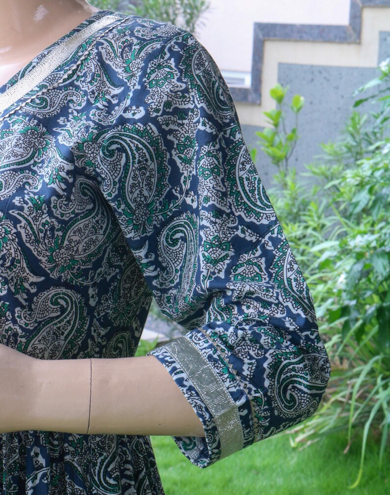 Puede incluir: Vestido azul marino con estampado de cachemira en verde y blanco. El vestido presenta un escote en V y mangas tres cuartos con ribete dorado. La tela tiene un patr&oacute;n detallado y repetitivo.