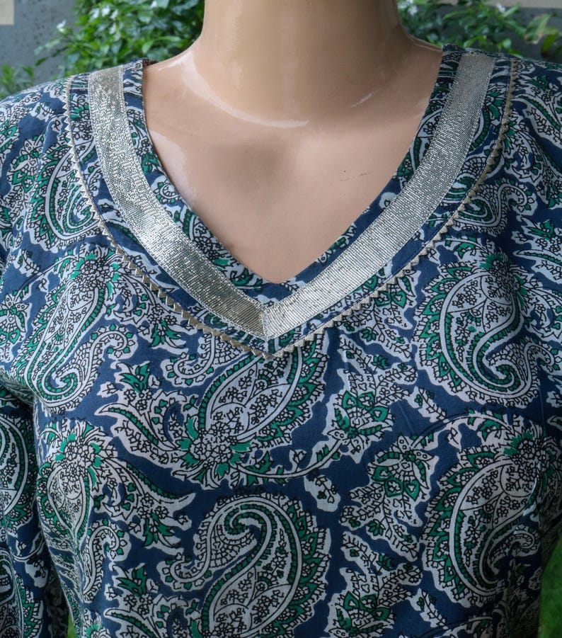Puede incluir: Top con cuello en V con estampado de cachemira en azul marino, blanco y verde. El escote est&aacute; adornado con una cinta plateada. La tela tiene un aspecto suave y fluido.
