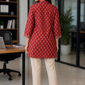 May include: A woman wearing a red tunic with a floral pattern and cream-colored pants. The tunic has three-quarter sleeves and a mandarin collar. The pants are straight-legged. The outfit is suitable for office wear.