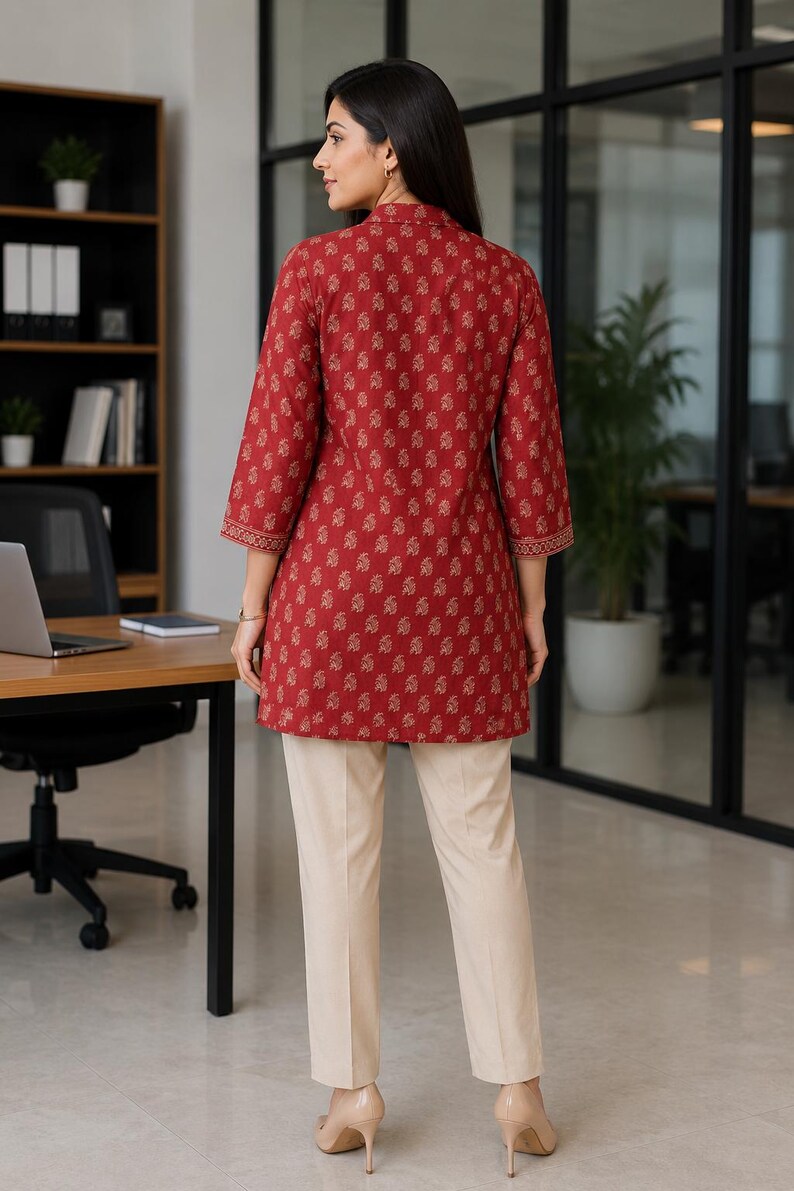May include: A woman wearing a red tunic with a floral pattern and cream-colored pants. The tunic has three-quarter sleeves and a mandarin collar. The pants are straight-legged. The outfit is suitable for office wear.