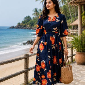 May include: A navy blue floral print midi dress with orange flowers and short sleeves. The dress has a V-neckline and a matching belt. A woven tote bag is carried. The background shows a beach scene with palm trees.