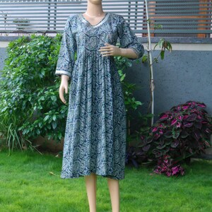 Puede incluir: Vestido largo sobre un maniqu&iacute;. El vestido es de color verde azulado oscuro con un estampado de cachemira en tonos verdes y blancos. Tiene un escote en V y mangas tres cuartos con ribete blanco. El vestido est&aacute; fruncido en la cintura y llega a la pantorrilla.