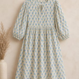 Flat lay view of women’s blue floral cotton midi dress featuring soft puff sleeves, gathered waistline, tie-up neckline, breathable lightweight fabric, and elegant handcrafted block print design — perfect boho summer dress for beach vacation and casual wear.