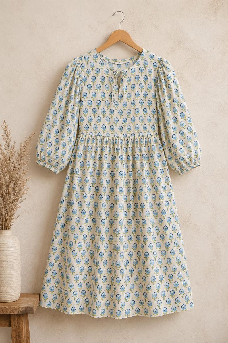 Flat lay view of women’s blue floral cotton midi dress featuring soft puff sleeves, gathered waistline, tie-up neckline, breathable lightweight fabric, and elegant handcrafted block print design — perfect boho summer dress for beach vacation and casual wear.