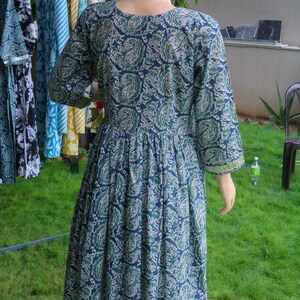 Puede incluir: Un vestido largo azul marino con un estampado de cachemira en tonos verdes y blancos. El vestido tiene mangas tres cuartos y cintura fruncida. El vestido se exhibe en un maniqu&iacute; al aire libre.