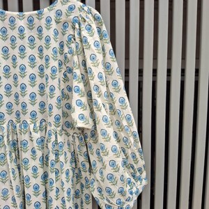 May include: A white dress with a blue floral pattern. The dress has long, puffy sleeves and a round neckline. The floral design is repeated across the fabric. The dress is made of a lightweight material.