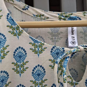 May include: Cream-colored top with a blue floral pattern and green leaves. The top has a keyhole neckline with a tie closure. The tag reads "fashion 21 M". The fabric is lightweight and appears to be cotton or a similar material.