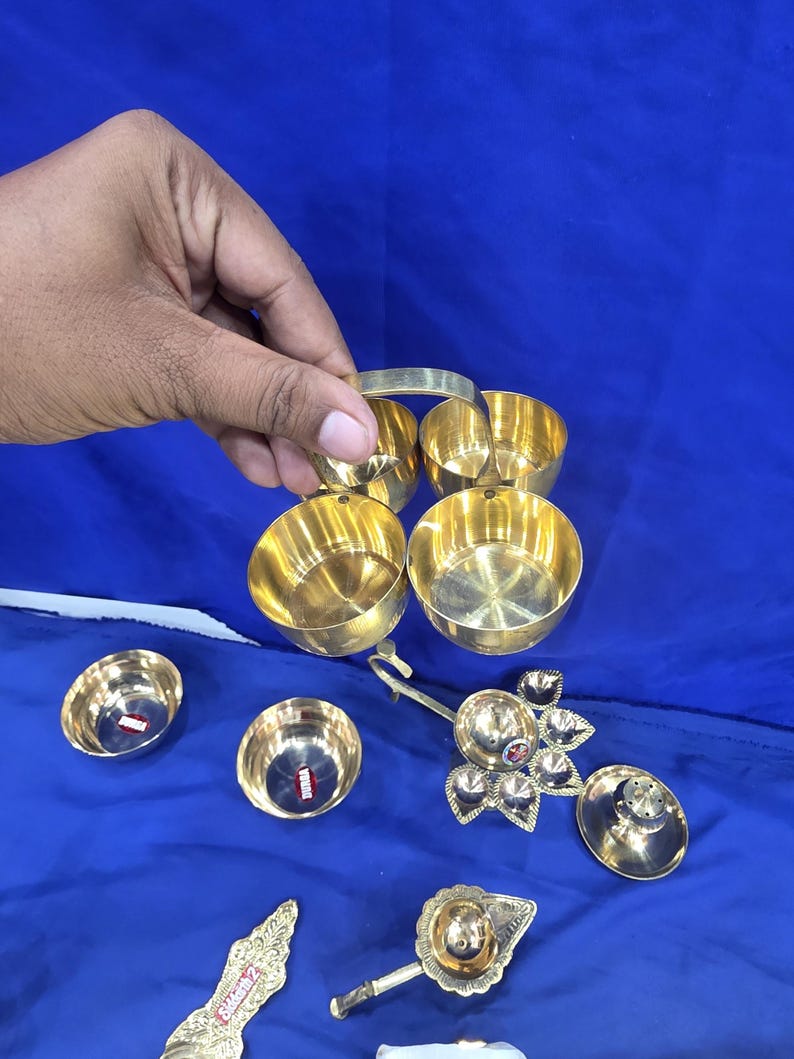 May include: A set of polished brass kitchenware items including a four-compartment bowl unit with a central handle, two individual small bowls, a multi-petaled oil lamp, a lidded container, a decorative spoon, and a small handled ladle.